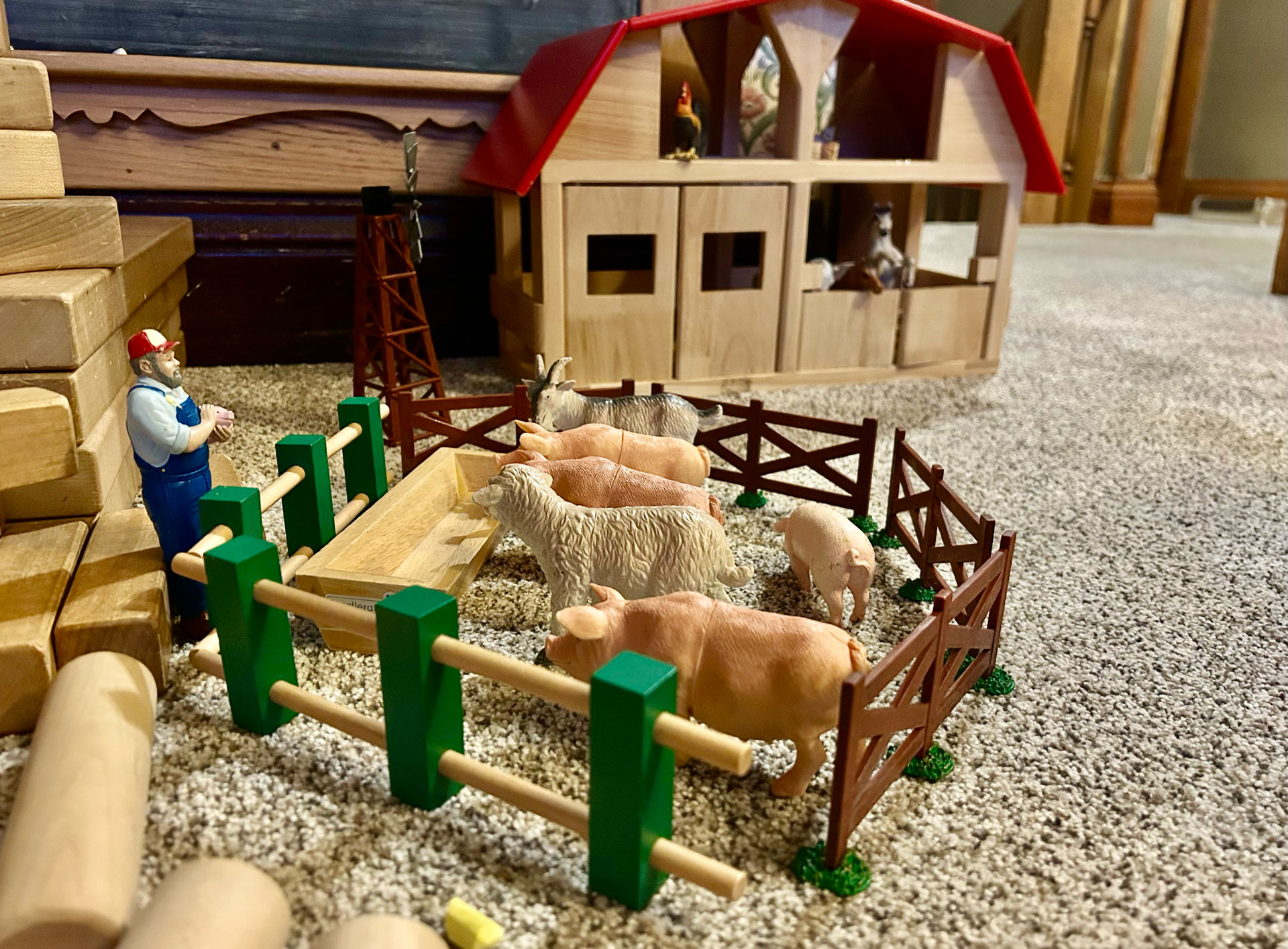 Wood and plastic farm toys depicting pigs and sheep in a pen near a barn